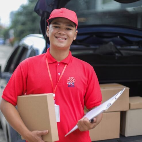 young-asian-delivery-man-in-red-uniform-holding-ca-2025-09-14-22-31-57-utc Smiling Young Asian Delivery Man In Red Uniform Holding Cardboard Box and Clipboard While Looking At Camera